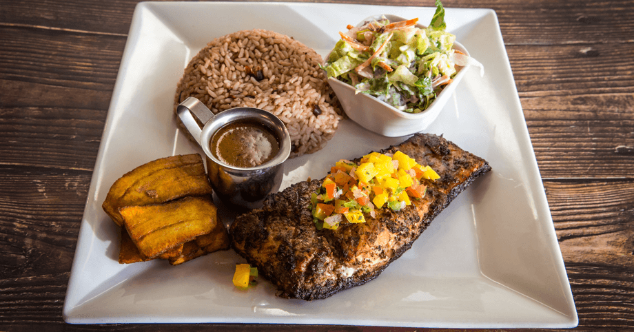 Bold Caribbean Flavors – Jerked Salmon with Mango Salsa & Classic Sides Jerked salmon topped with mango salsa, served with rice & peas, plantain, and fresh salad