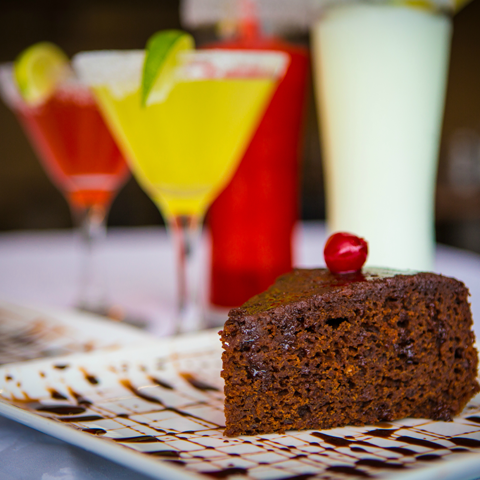 Click to view full image of Jamaican rum cake Jamaican rum cake with drinks in the background – thumbnail view