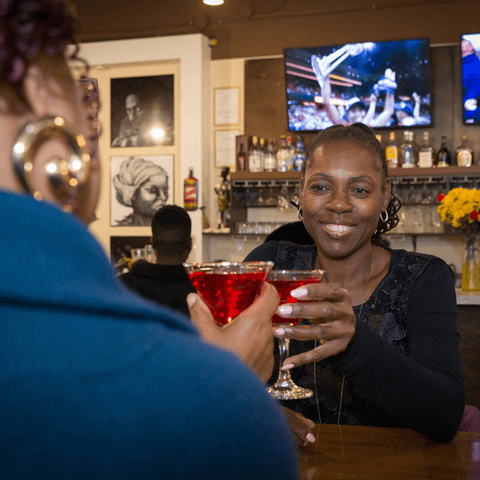 Click to view full image of friends enjoying cocktails at the bar Two women enjoying cocktails while watching the game at the bar – thumbnail view